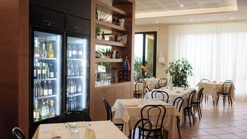 A restaurant with tables and chairs, a refrigerator with bottles, and a plant.