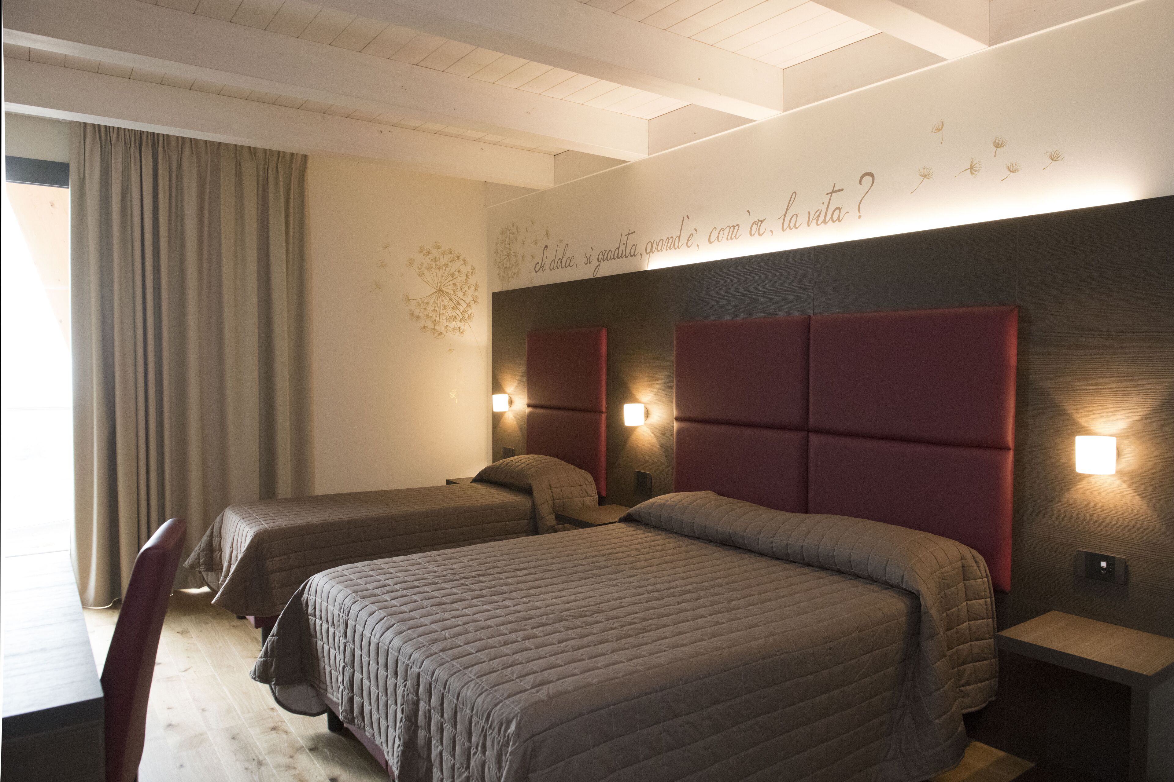 Habitación de hotel con dos camas, un escritorio y una silla. Hay apliques a ambos lados de las camas y una lámpara de pared sobre la cama a la derecha.