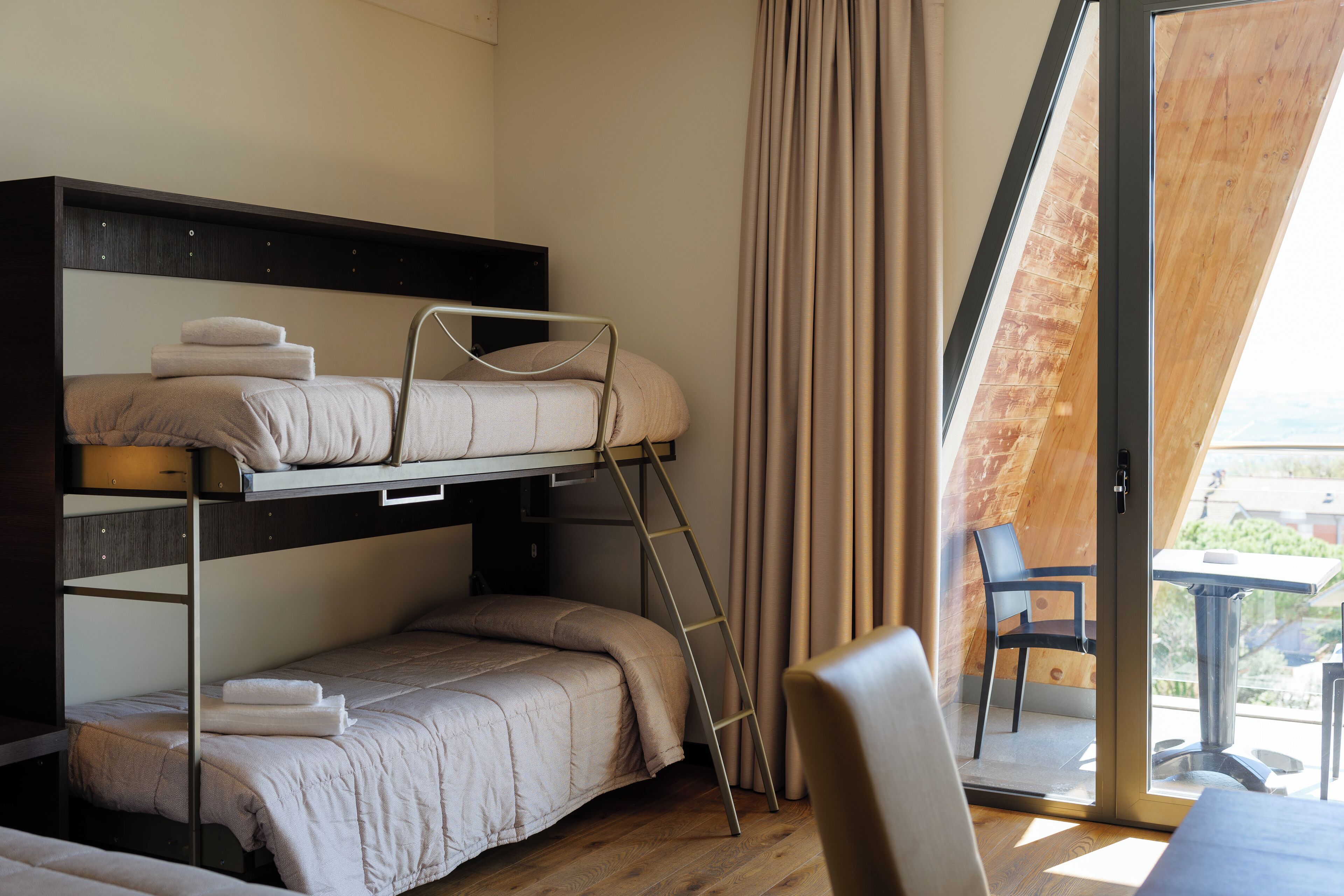 Une chambre avec un lit superposé, une échelle, une chaise et une table près d’une porte-fenêtre coulissante.
