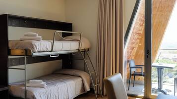 A bunk bed room with a ladder, a chair, and a table by a sliding glass door.