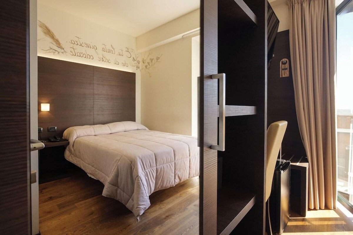 A bedroom with a bed, a bedside table, a TV, and a window with curtains.
