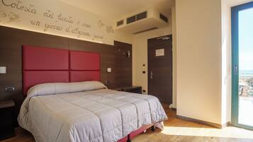 Un dormitorio con cabecera roja, cama con cubrecama gris, suelo de madera y pared con una frase decorativa.