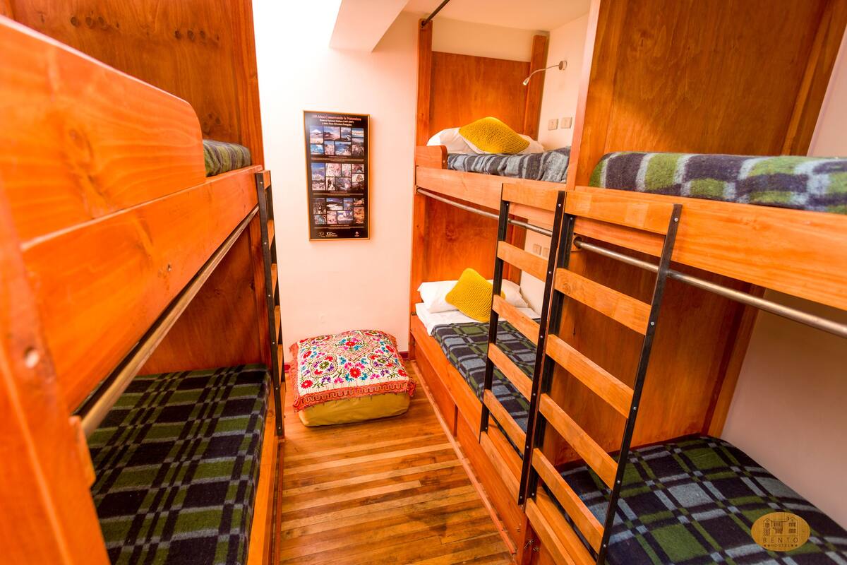A narrow room with bunk beds, a small table with a floral cushion, and a framed photo on the wall.