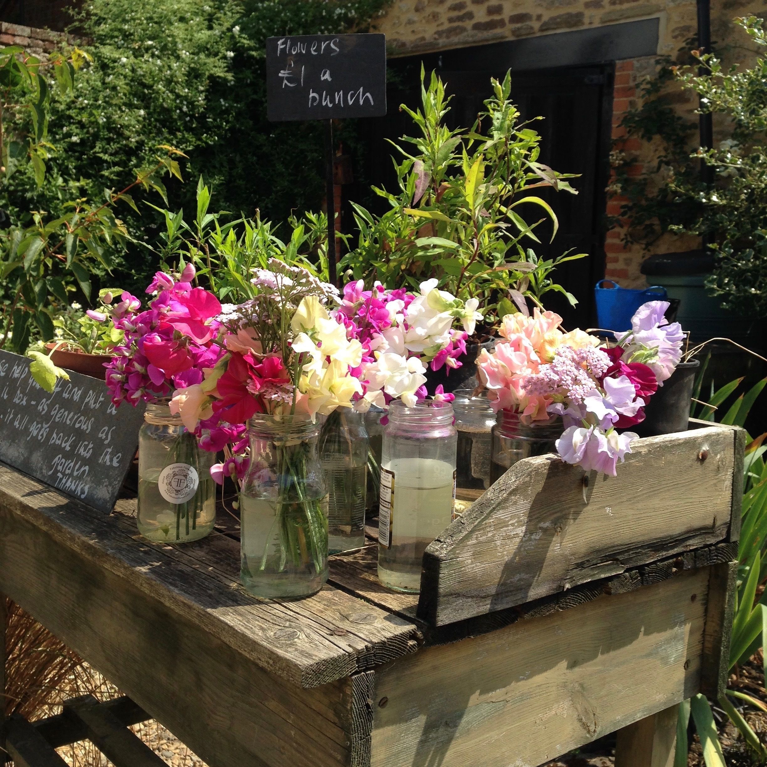 A wooden bench with jars of flowers for sale.