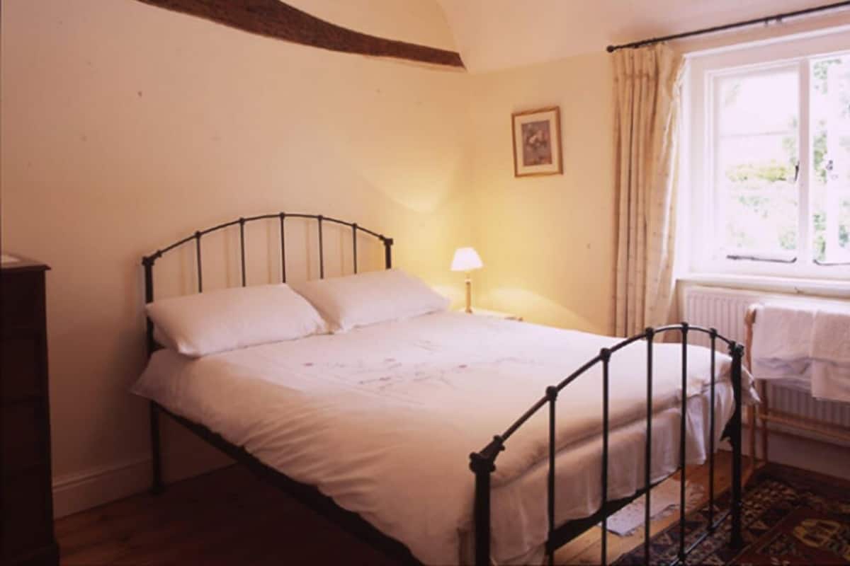Una camera da letto con un letto singolo, un comodino, una lampada, una finestra con tende e un termosifone.