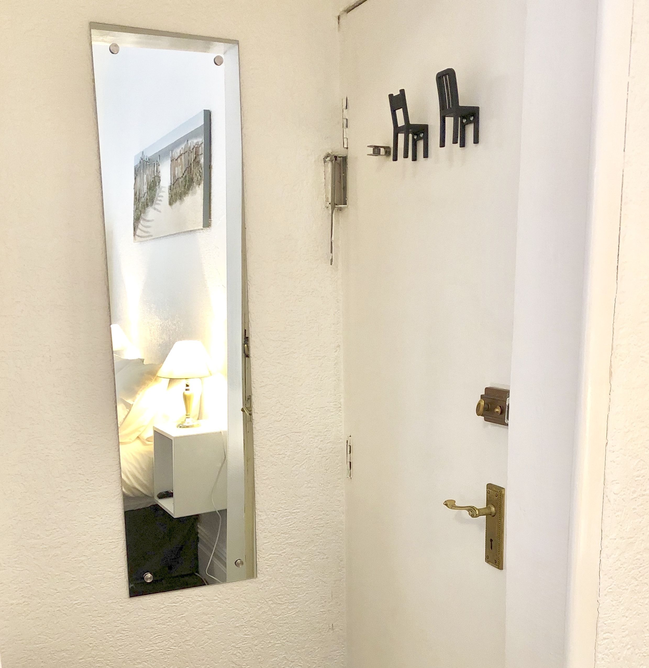 Une porte blanche avec un miroir, une poignée de porte en laiton et deux chaises noires fixées au mur.
