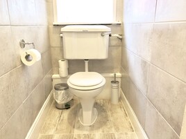 Een standaard badkamer met toilet, toiletpapier, een prullenbak en een douchetoilet.