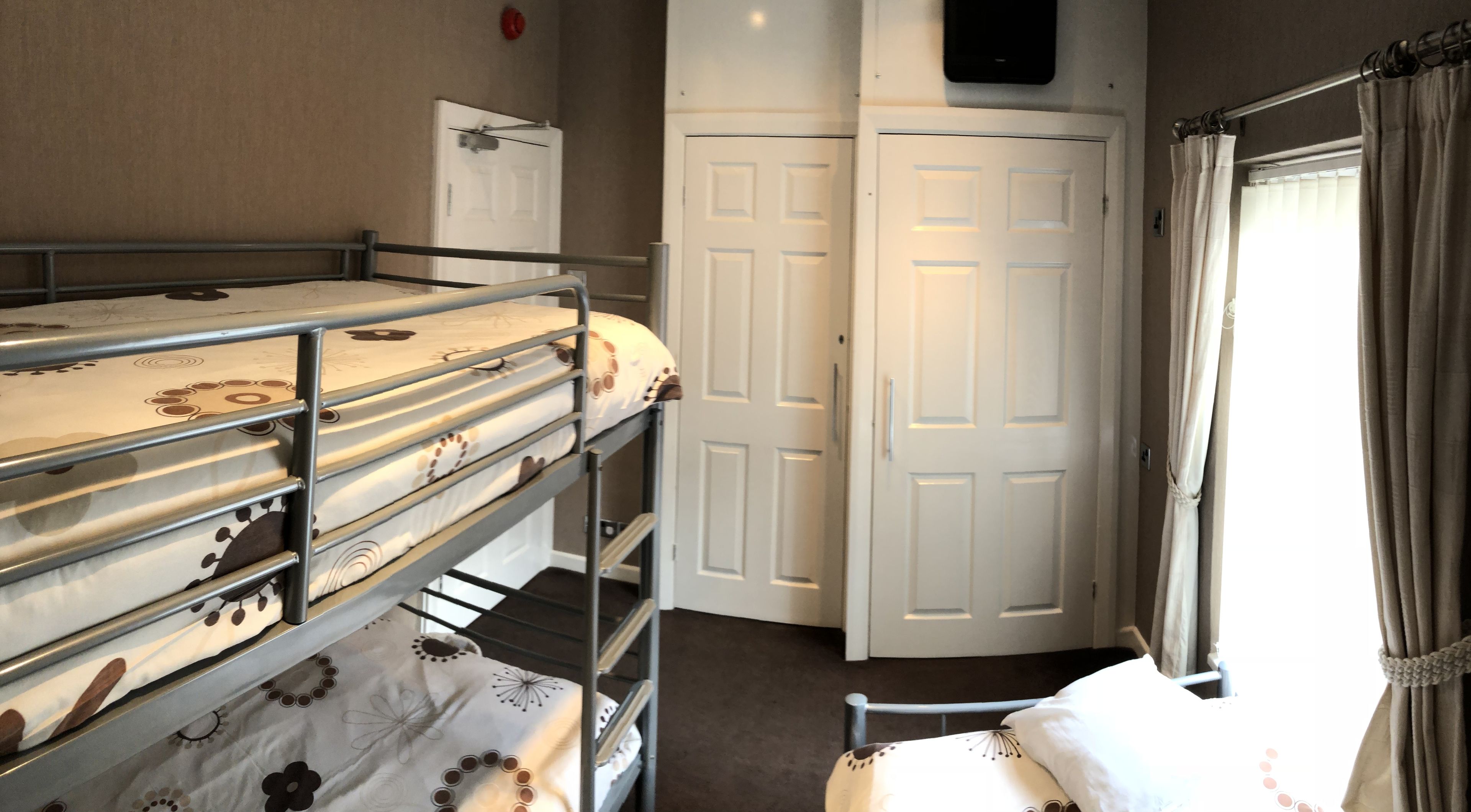 Een slaapkamer met een stapelbed, een deur en een raam met gordijnen.