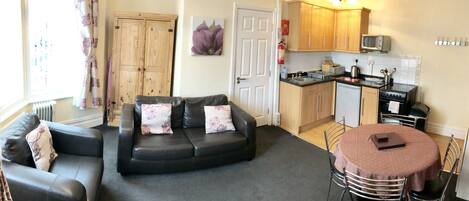 A compact living space with a sofa, a dining table, a kitchenette, and a door leading to another room.