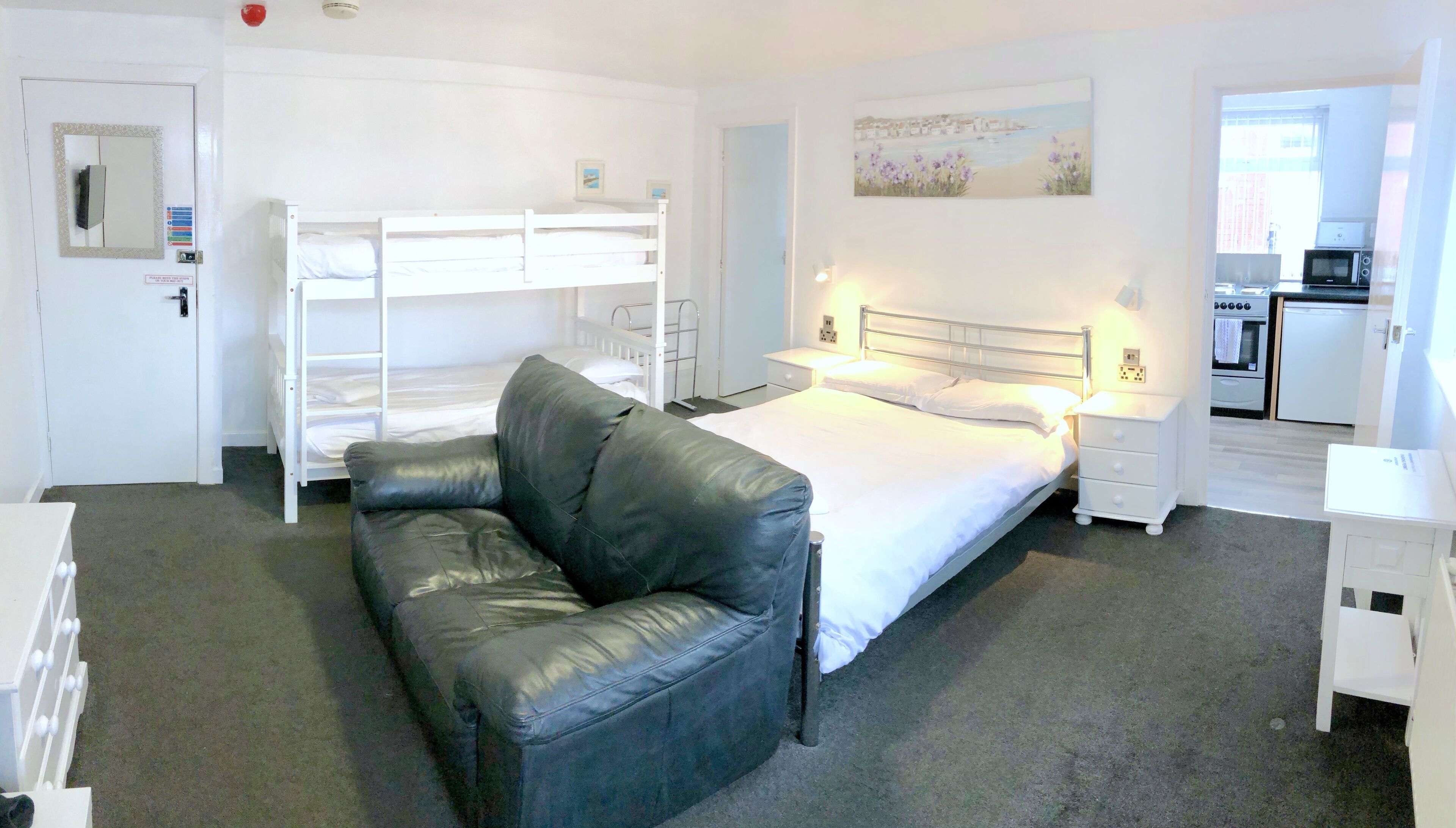 Une chambre avec un lit superposé, un lit simple, un canapé en cuir noir, une table de chevet, une commode et un petit bureau blanc.