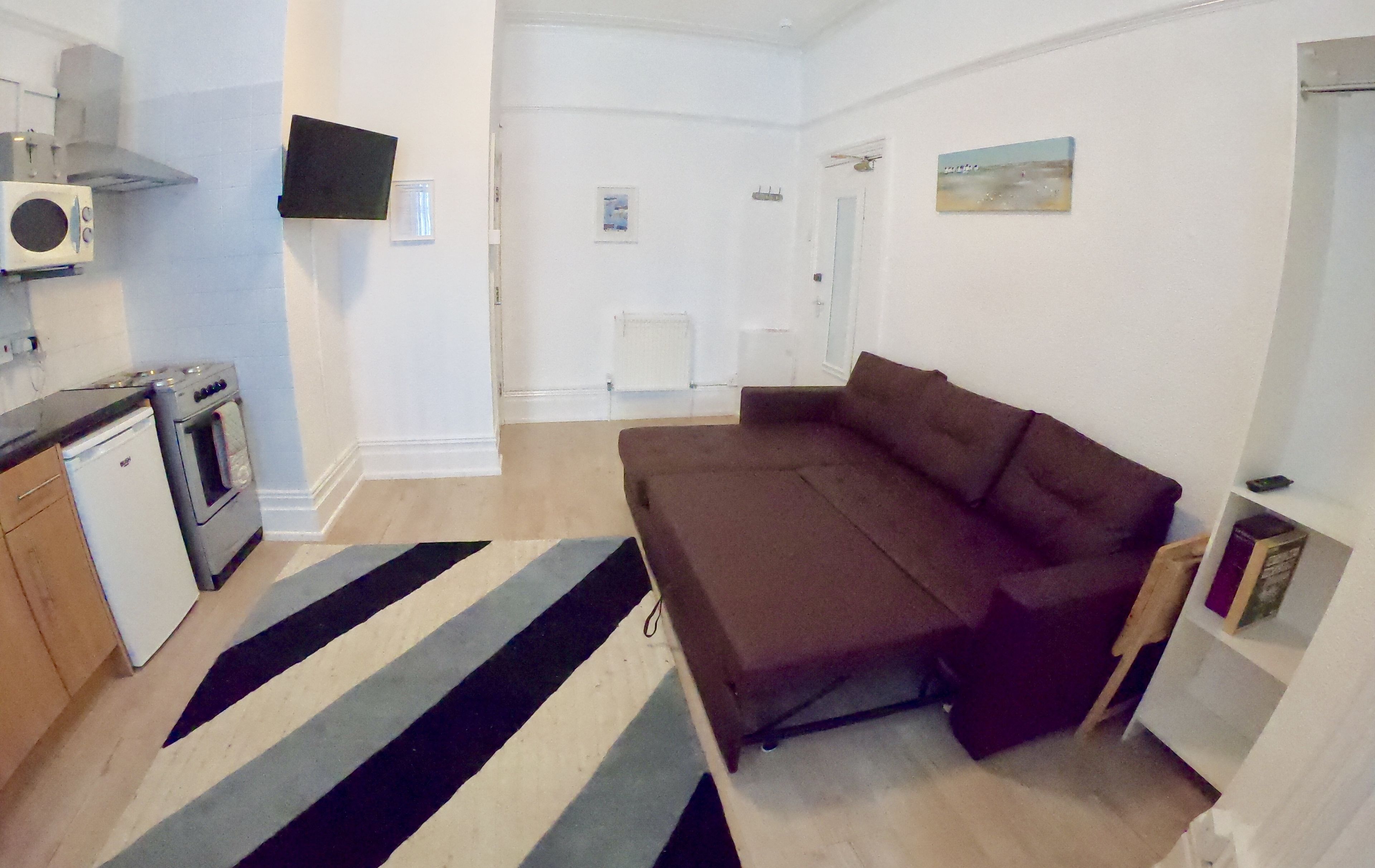 A compact living space with a kitchenette, a sofa, and a striped rug.