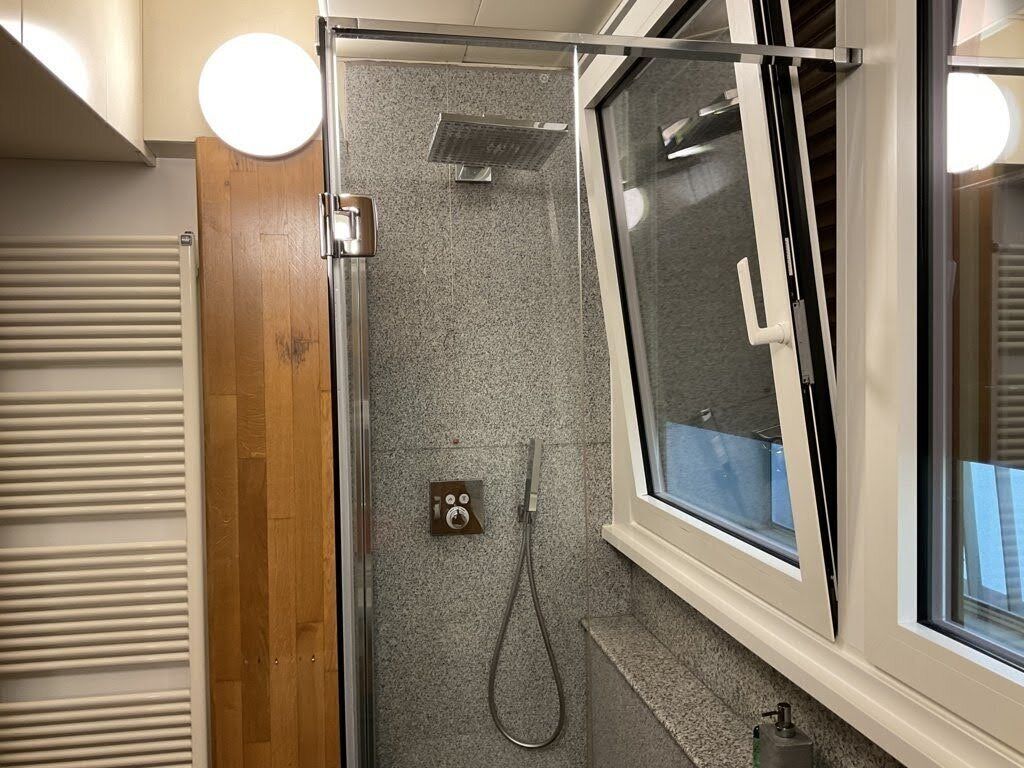 A shower with a glass door, a control panel, and a window.