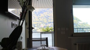 A room with a view of a lake and hills, a dining table with a glass centerpiece, and a chair. - Lakeviewcabin - King Room With Balcony (Como)