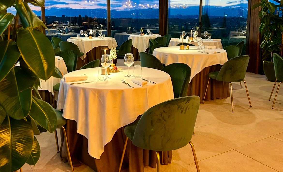 A restaurant with round tables and chairs, set against a backdrop of a scenic view.