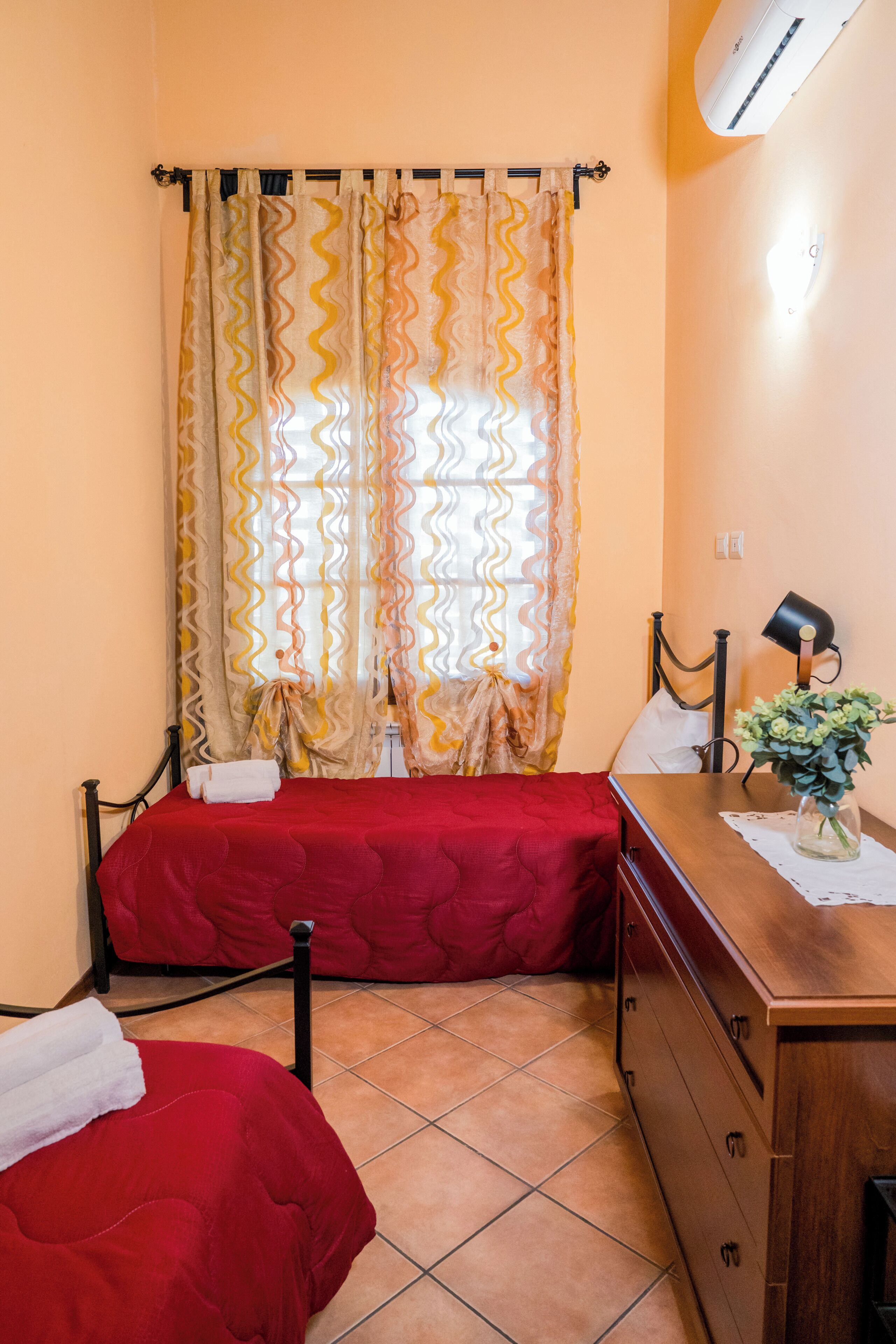 A room with two beds, a wooden dresser, a desk with a lamp, and a window with curtains.