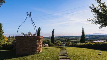 A stone structure with a metal archway, surrounded by a grassy area with a clear path leading to a distant view of rolling hills and a body of water.