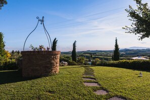A stone structure with a metal archway, surrounded by a grassy area with a clear path leading to a distant view of rolling hills and a body of water.