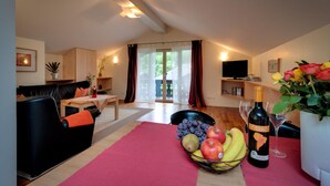 Una sala de estar moderna con un sofá, una mesa de comedor con fruta y vino, y vistas a través de un ventanal.