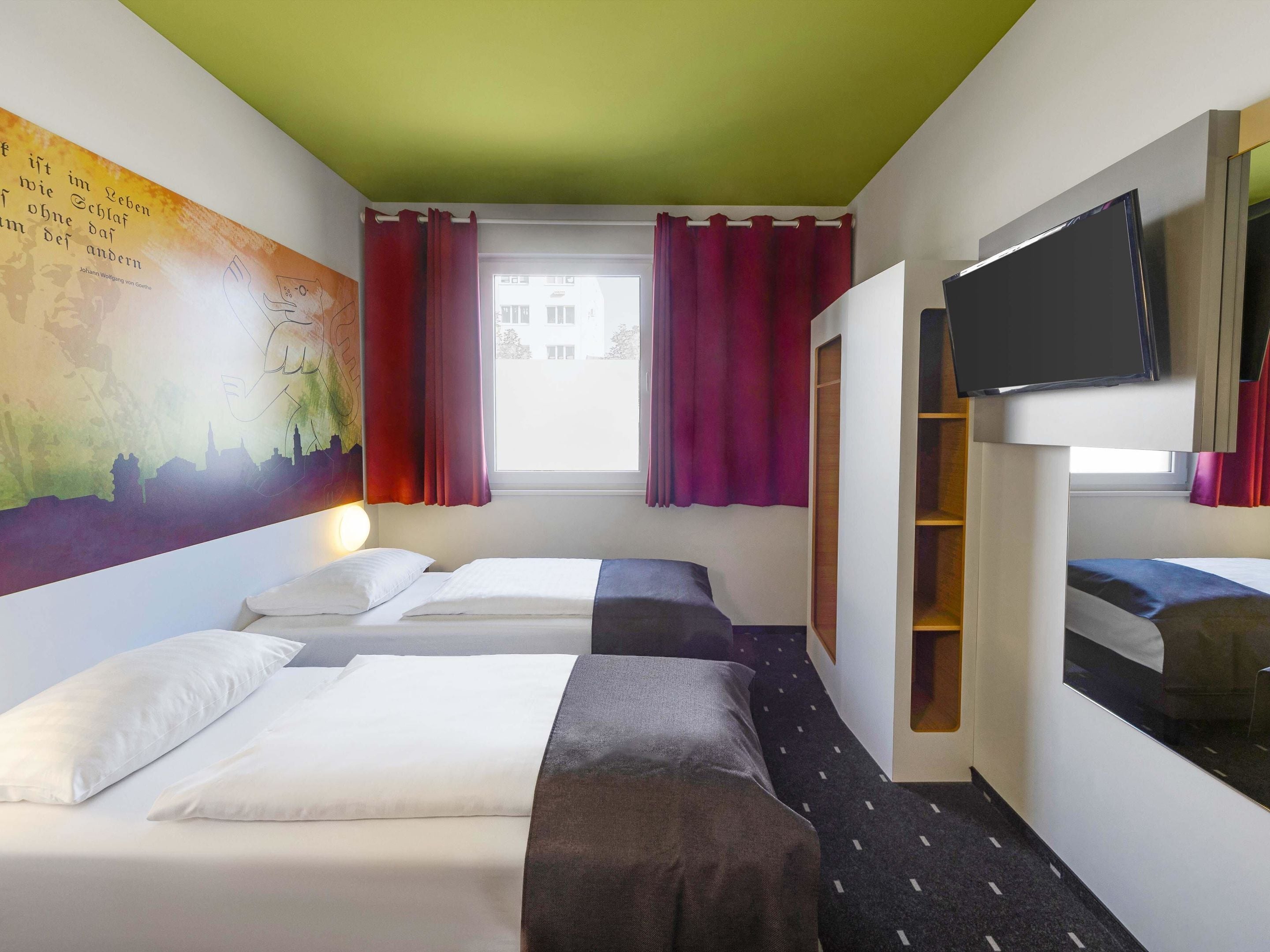 A hotel room with two beds, a TV, a mural, and a window with curtains.
