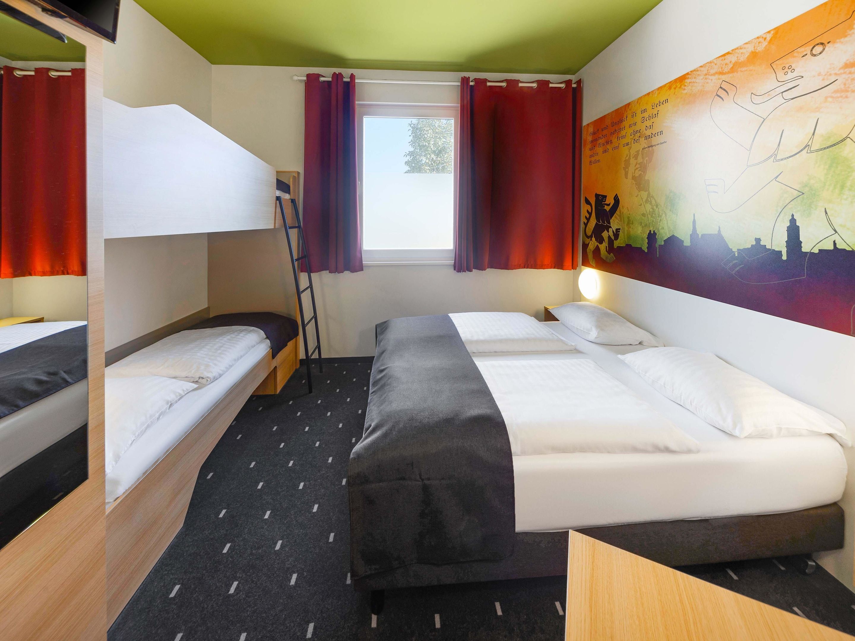 Ein Zimmer mit Etagenbetten, einer Leiternetzung, einem Fenster mit Vorhängen und einem Stadtbild-Wandgemälde.