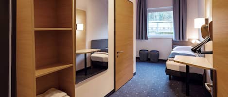 Quarto de hotel com cama, escrivaninha, cadeira, espelho e guarda-roupa.