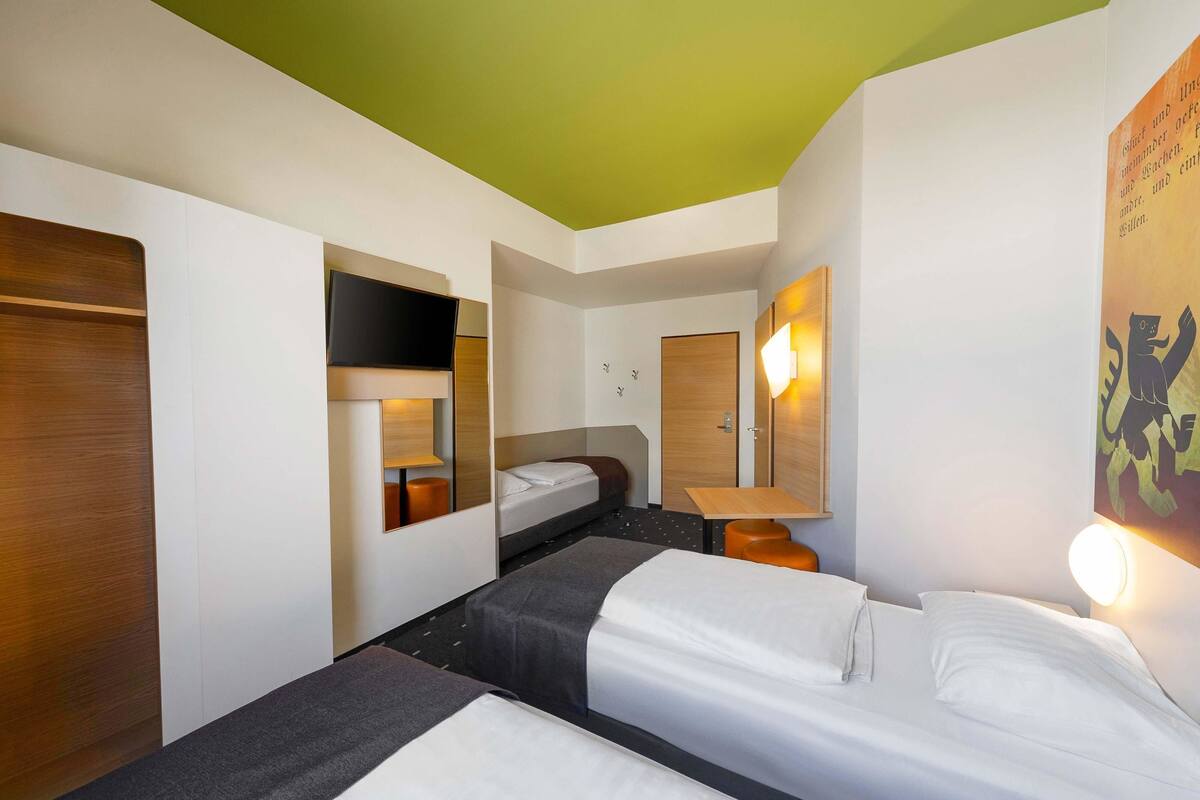 A hotel room with two beds, a television, a mirror, and a wall-mounted light.