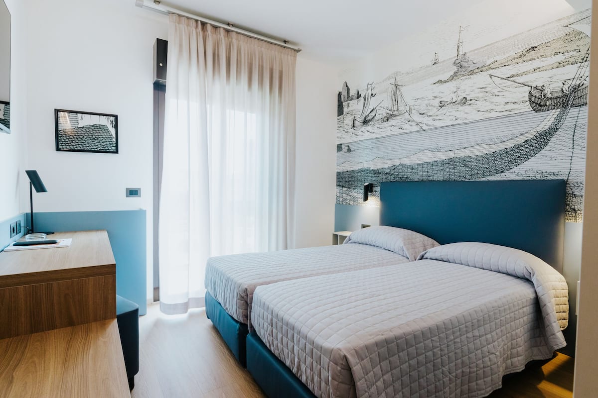 A modern hotel room with two beds, a desk, and a large nautical-themed wall mural.