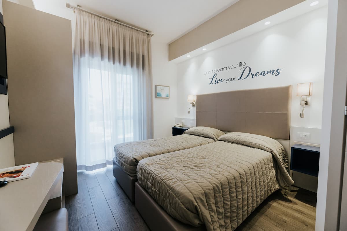 A modern hotel room with a large bed, bedside tables, a desk, and a motivational wall quote.