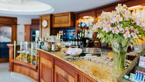 Un espace bar avec un comptoir en bois, un vase de fleurs et diverses bouteilles et verres.