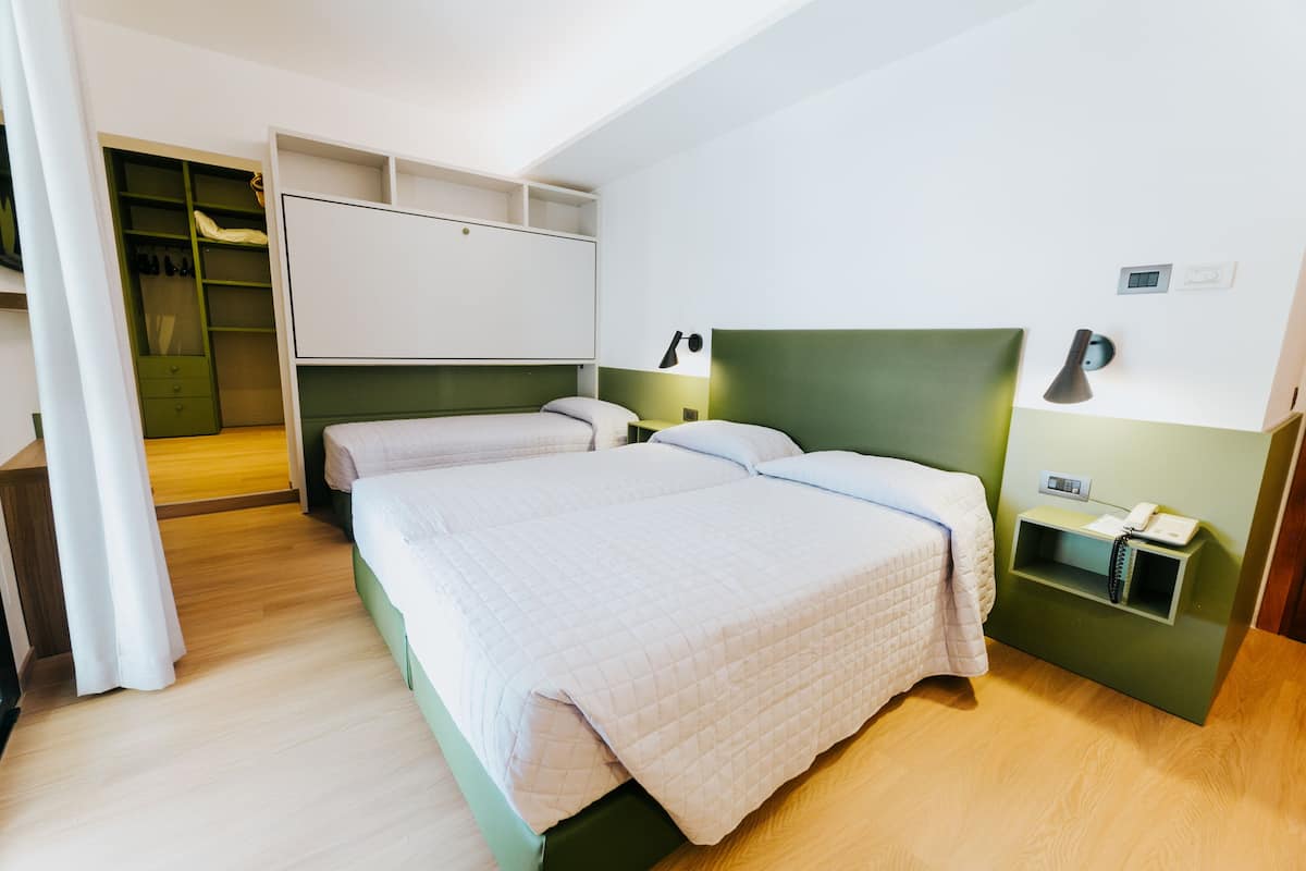 A bedroom with two beds, a walk-in closet, and a bedside table with a lamp.