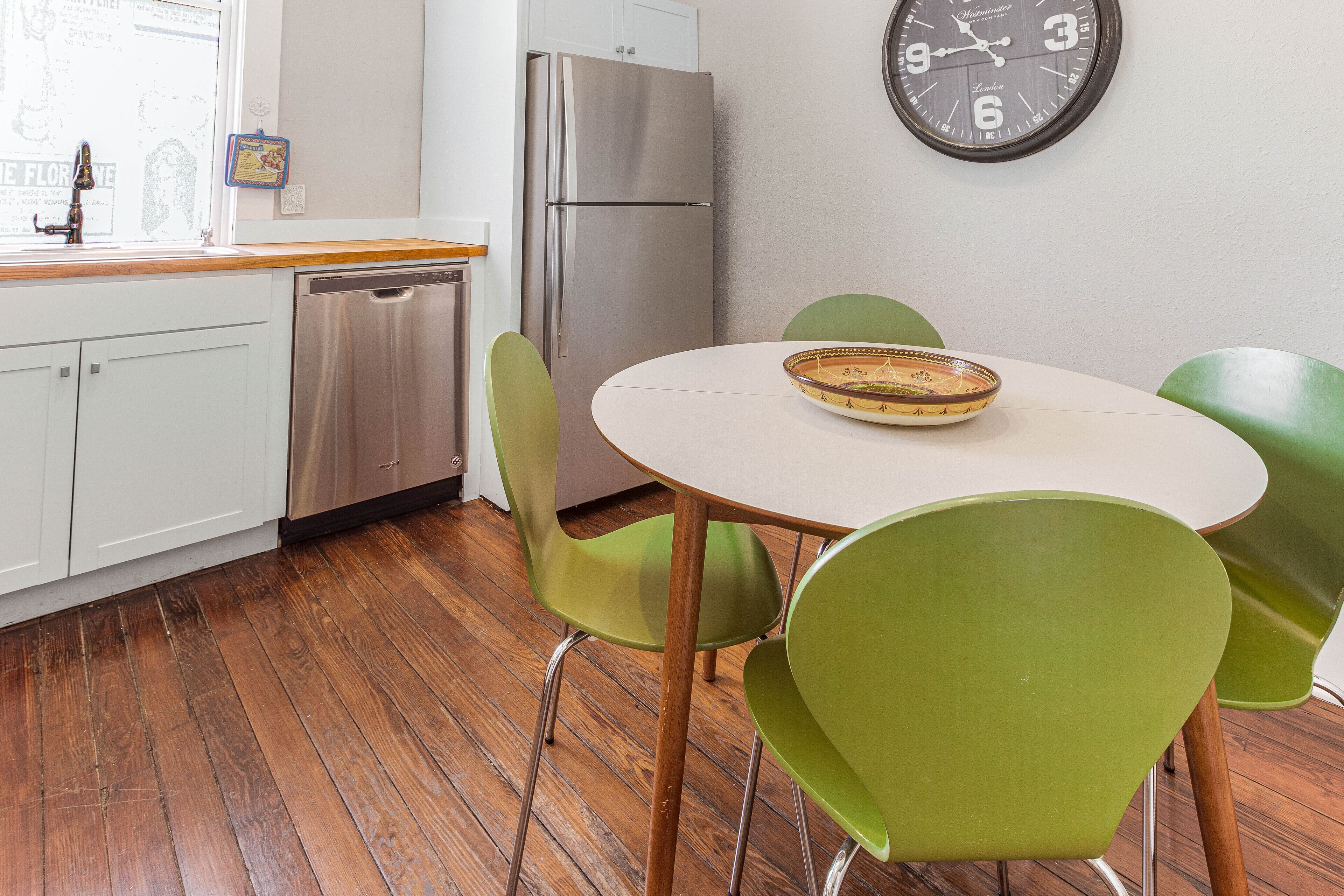 Una cocina moderna con un refrigerador de acero inoxidable, un lavavajillas y una mesa redonda con un tazón encima.