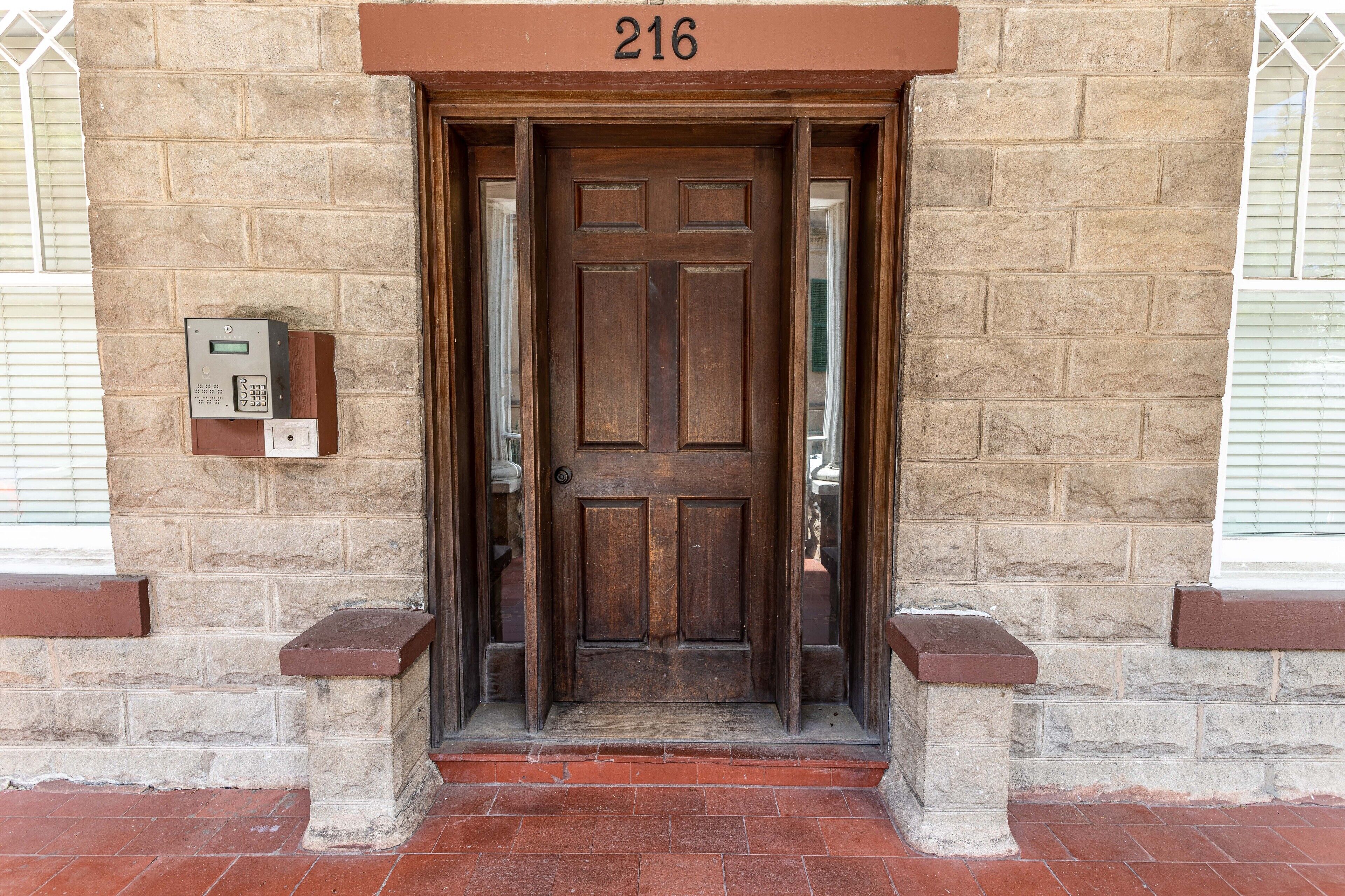 A wooden door with a number plate reading 216, a keypad, and a small step leading up to the entrance.