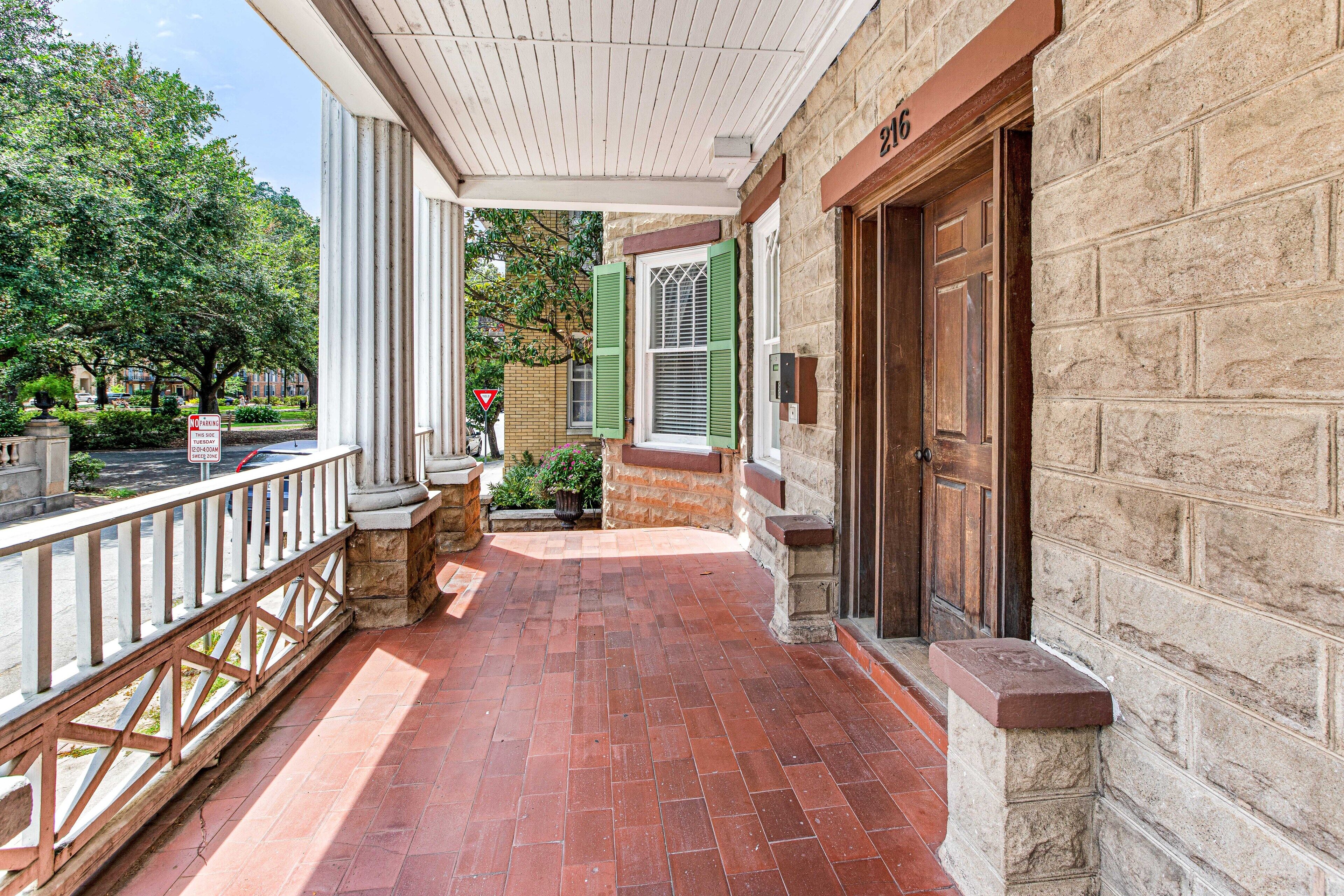 A covered porch with a brick floor, a wooden railing, and a stone wall.