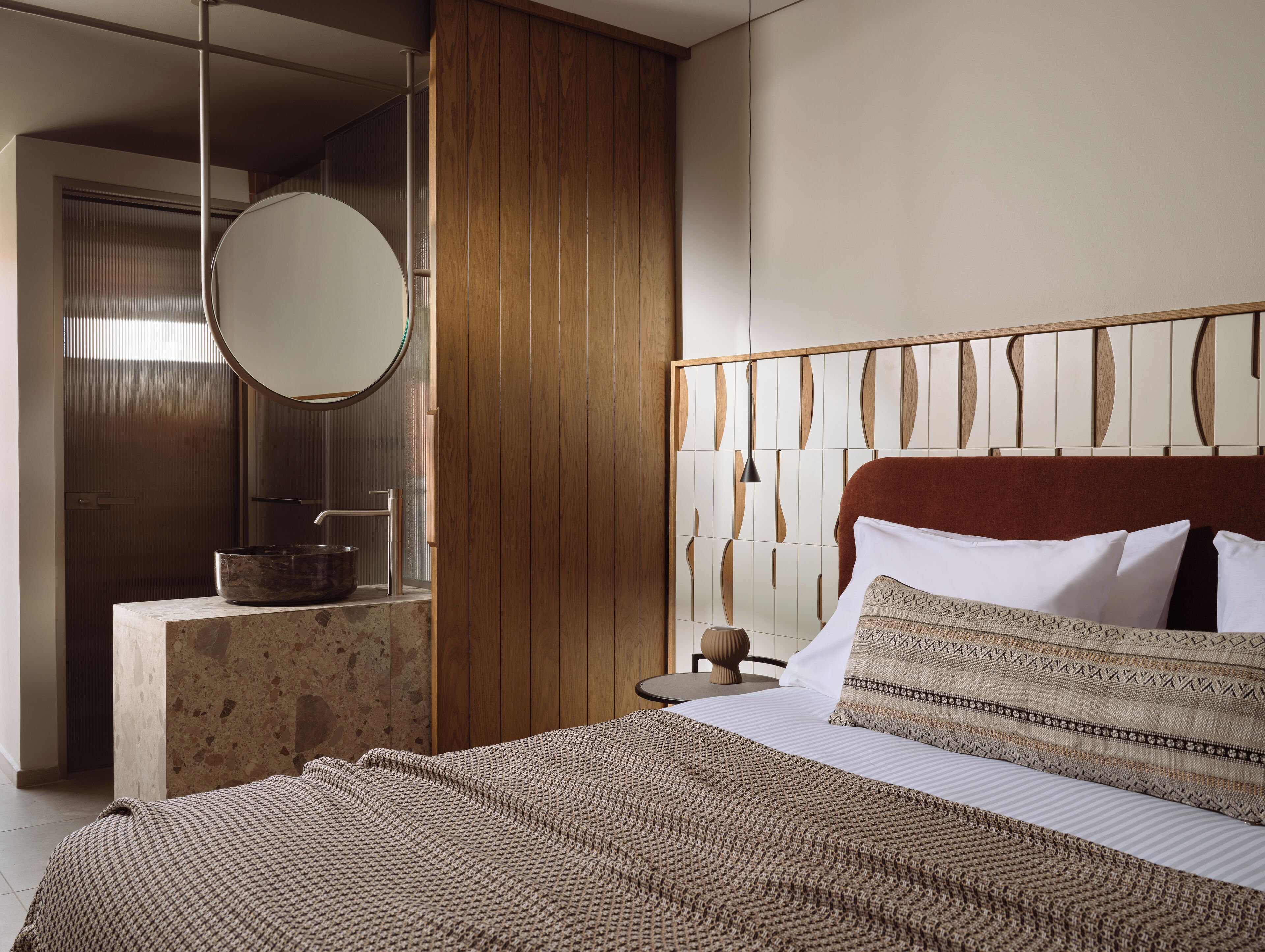 Une chambre à coucher moderne avec un grand lit, une tête de lit en bois, un miroir rond et une petite table de chevet.