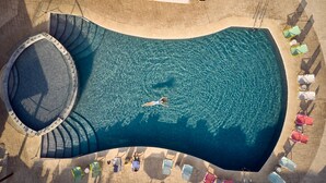 Vista aérea de una piscina con diseño curvo, rodeada de sillones de descanso y una tumbona.