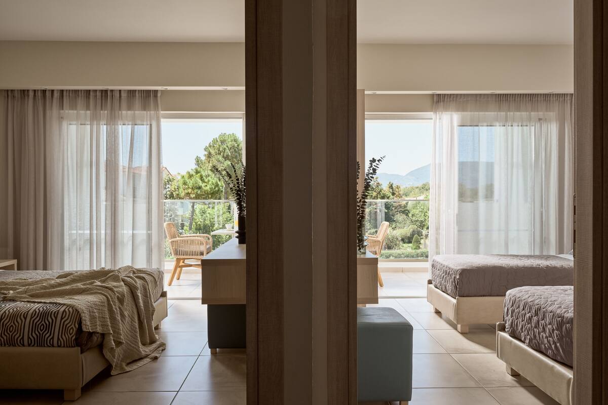 A modern bedroom with a large bed, a smaller bed, and a seating area with a view of the outdoors.