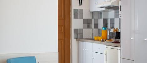 A modern kitchen with white cabinets, a blue chair, and a bed in the foreground.