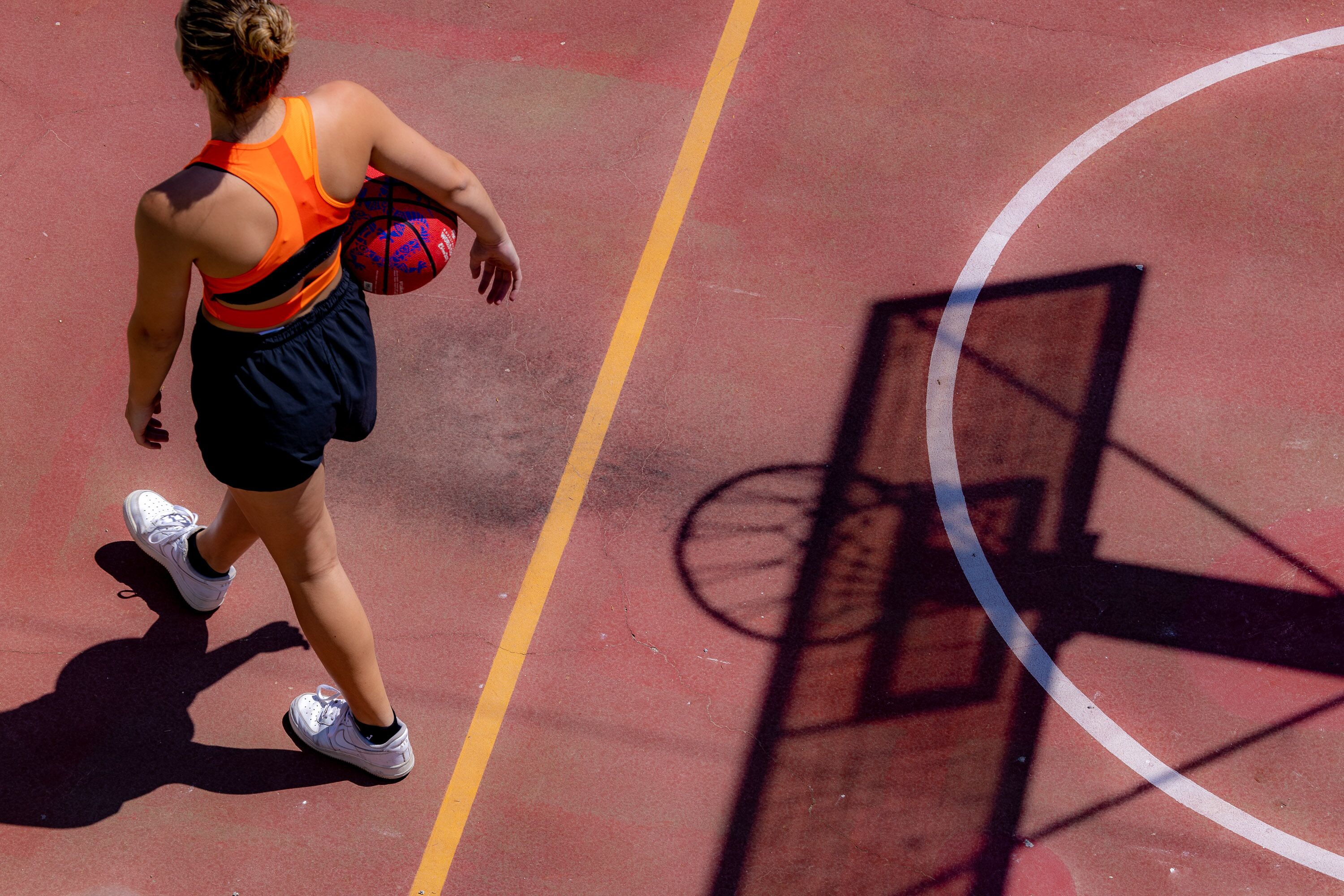 A basketball court with a player in motion, a hoop, and a shadow of a basketball net.
