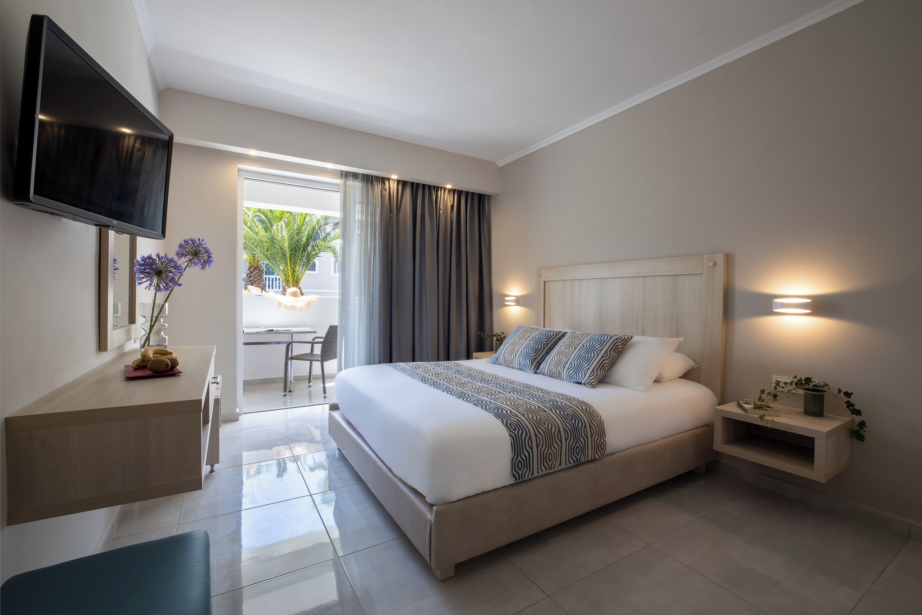 Una habitación de hotel moderna con una cama grande, un escritorio, un televisor y vistas al exterior.