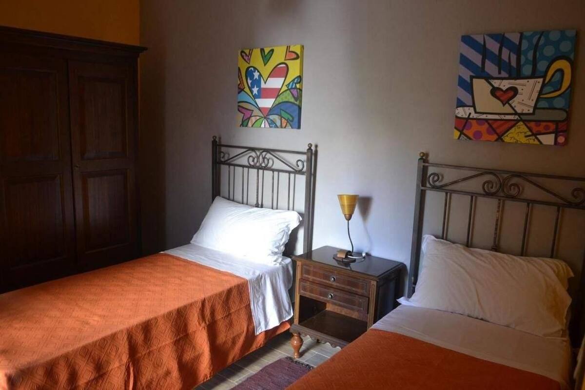 A room with two single beds, wooden wardrobe, and two paintings on the wall.