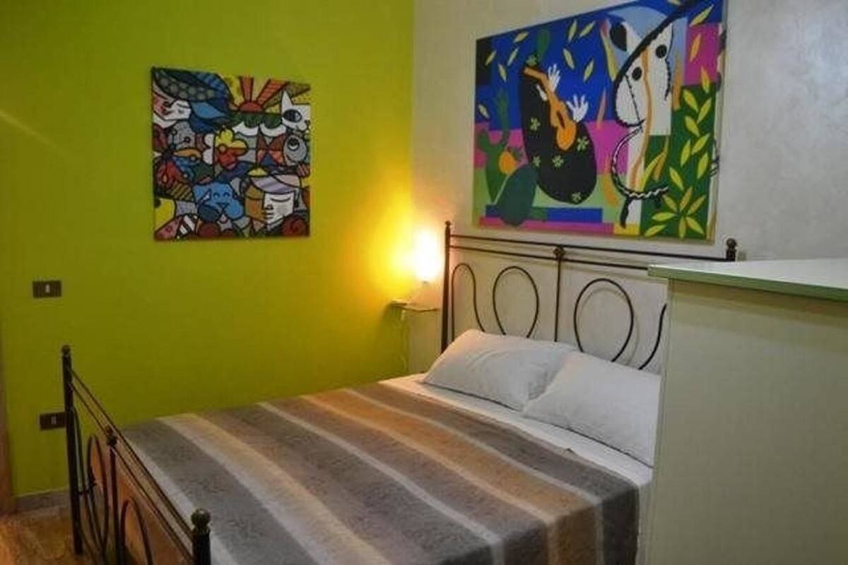 A room with a bed, a metal headboard, and two paintings on the wall.