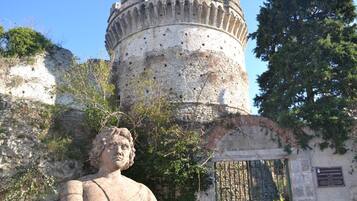 Una estatua de piedra frente a un edificio histórico con una torre redonda y un portón verde.