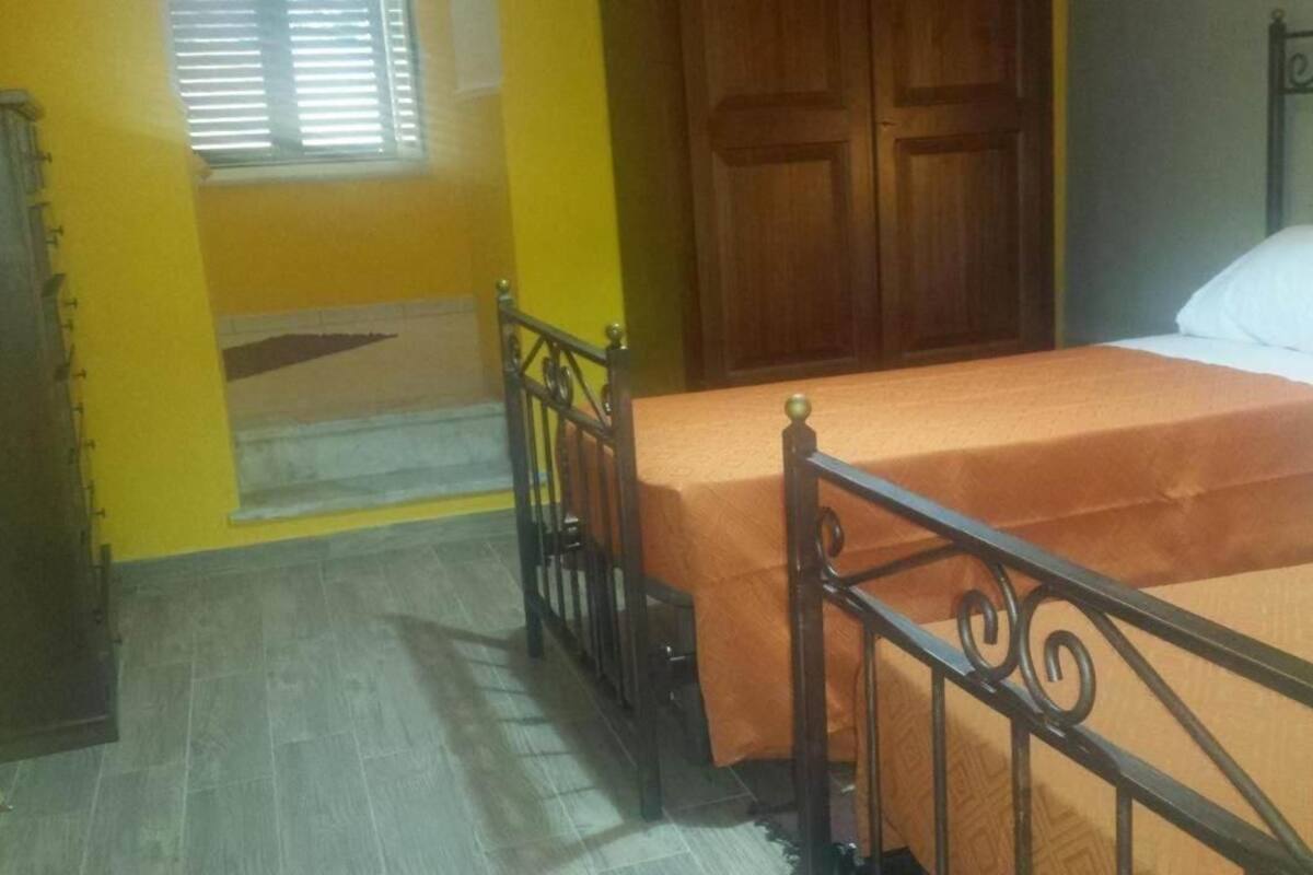 A room with two beds, a wooden door, and a window with blinds.