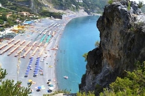 A coastal beach with rows of umbrellas and sun loungers, a rocky cliff, and a clear blue sea. - La Marinella (Belvedere Marittimo)