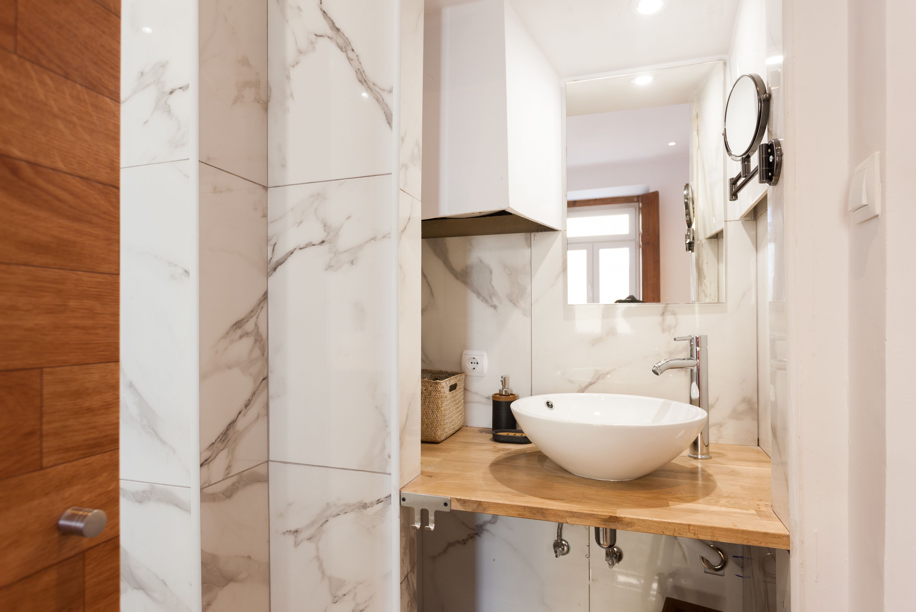 Een moderne badkamer met een groot wit wastafelmeubel, marmeren tegels en een houten opbergmeubel.