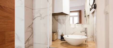 Une salle de bain moderne avec un grand lavabo blanc, des carreaux de marbre et un meuble-lavabo en bois.