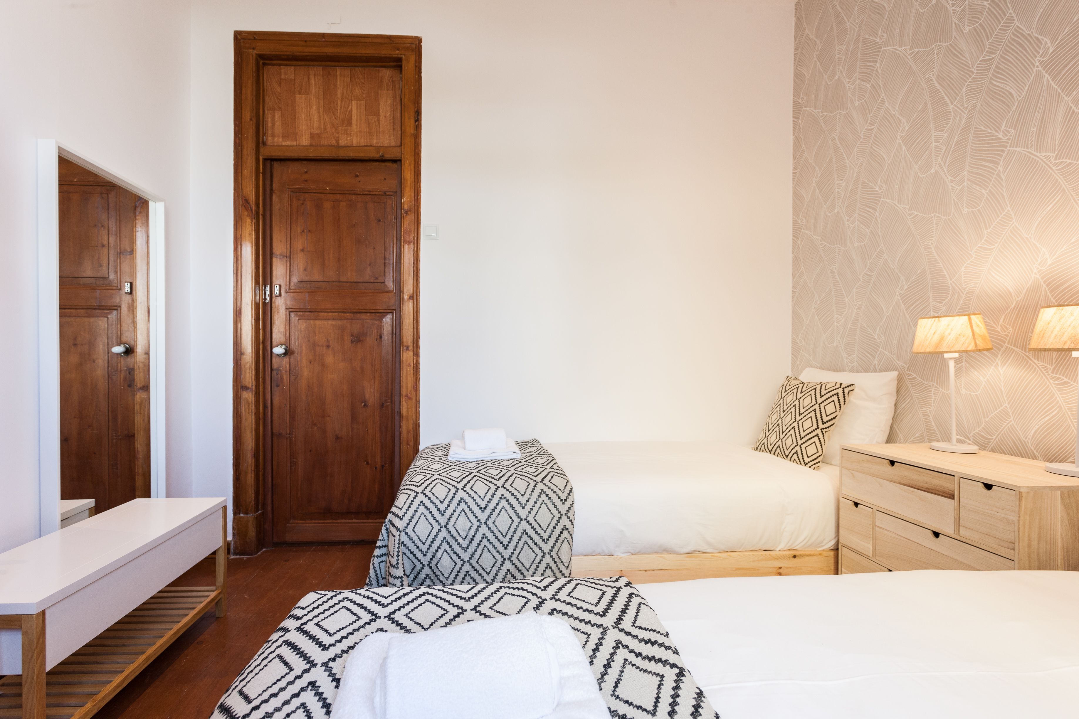 Ein Schlafzimmer mit Holzschrank, Nachttisch, Lampe und einem Bett mit Musterdecke.