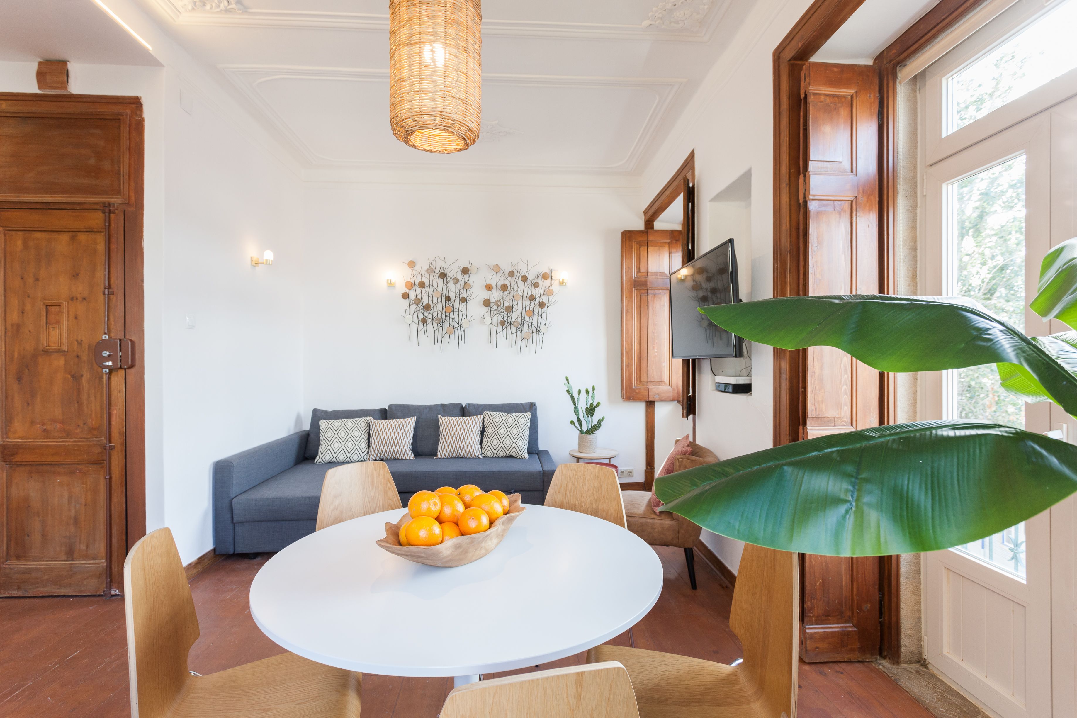 Un coin repas avec une table ronde, des chaises et un saladier rempli d’oranges.