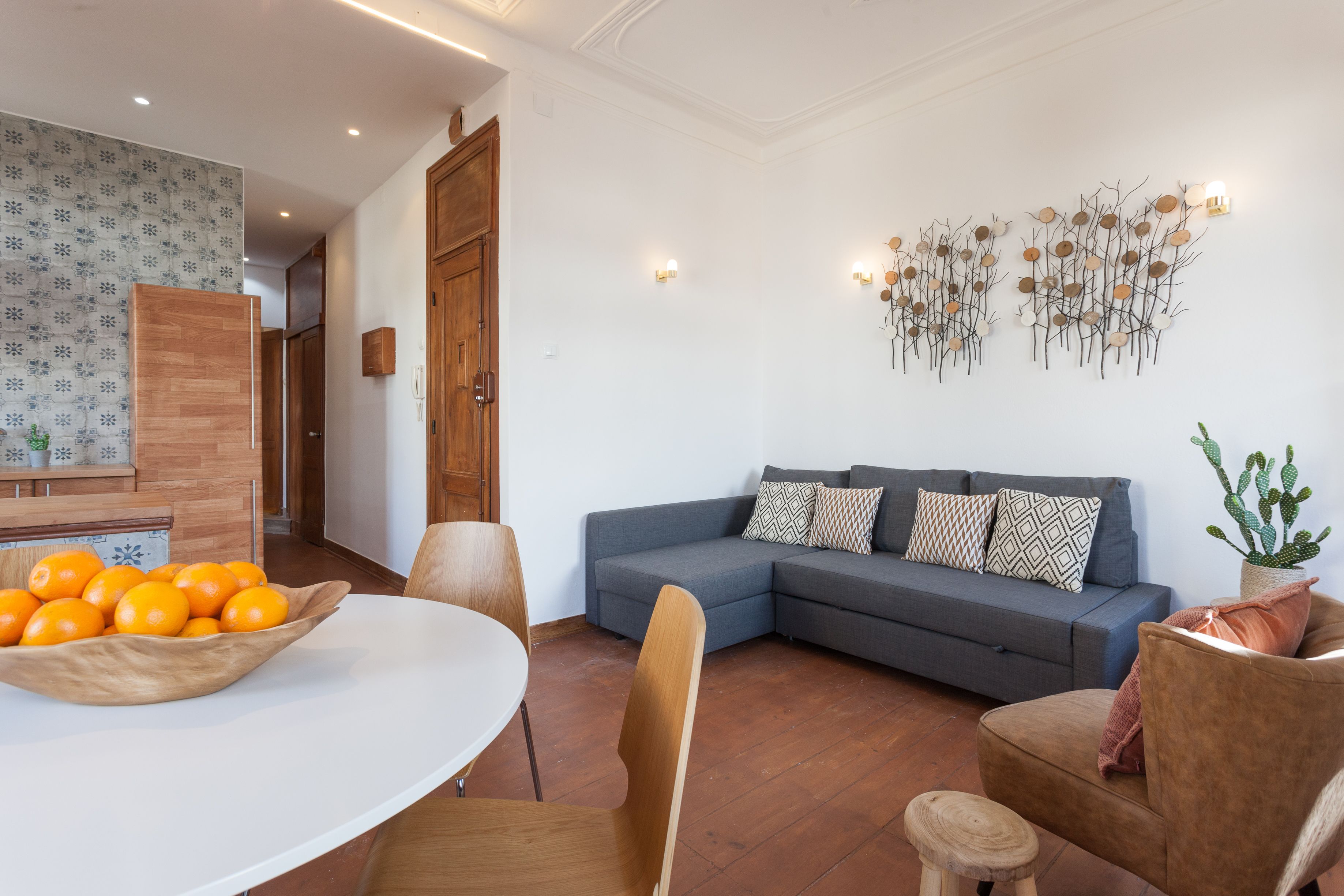 Een moderne woonkamer met een grijze hoekbank, een houten eettafel en een schaal mandarijnen.