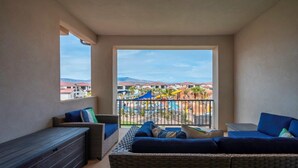 Un balcone con mobili in vimini, vista su un resort con piscine e ombrelloni, e montagne sullo sfondo.